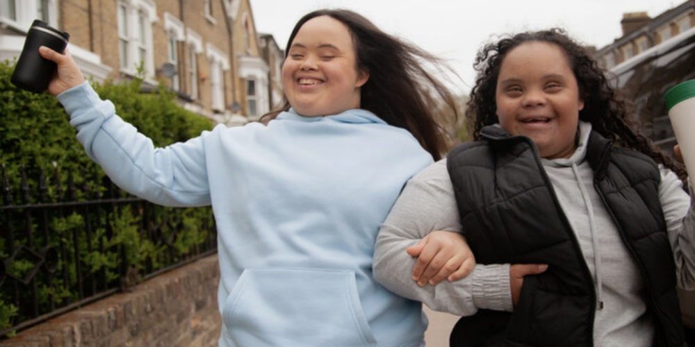 two young adults with developmental disabilities with linked arms skipping through the street in honor of Developmental Disabilities Month