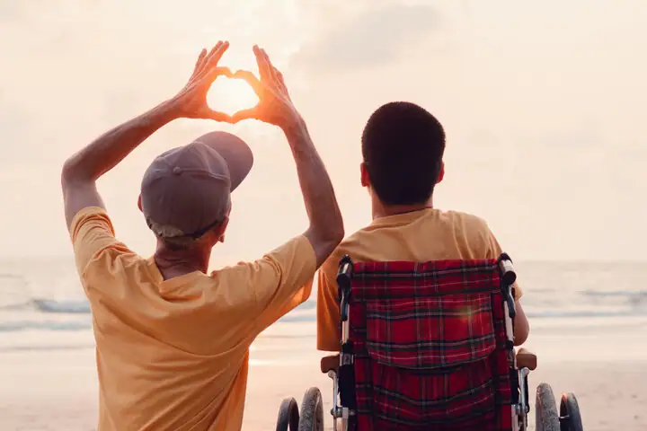 Father and his disabled son traveling for the summer at the beach with his son in his wheelchair