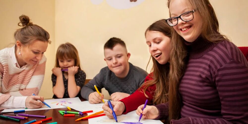 5 students with various intellectual or developmental disabilities around a school table working on an art project