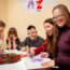 5 students with various intellectual or developmental disabilities around a school table working on an art project