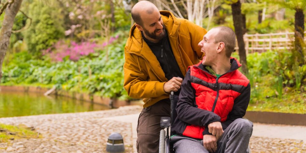 Father with adult child with developmental disability in his wheelchair on an accessible path in the park