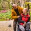 Father with adult child with developmental disability in his wheelchair on an accessible path in the park